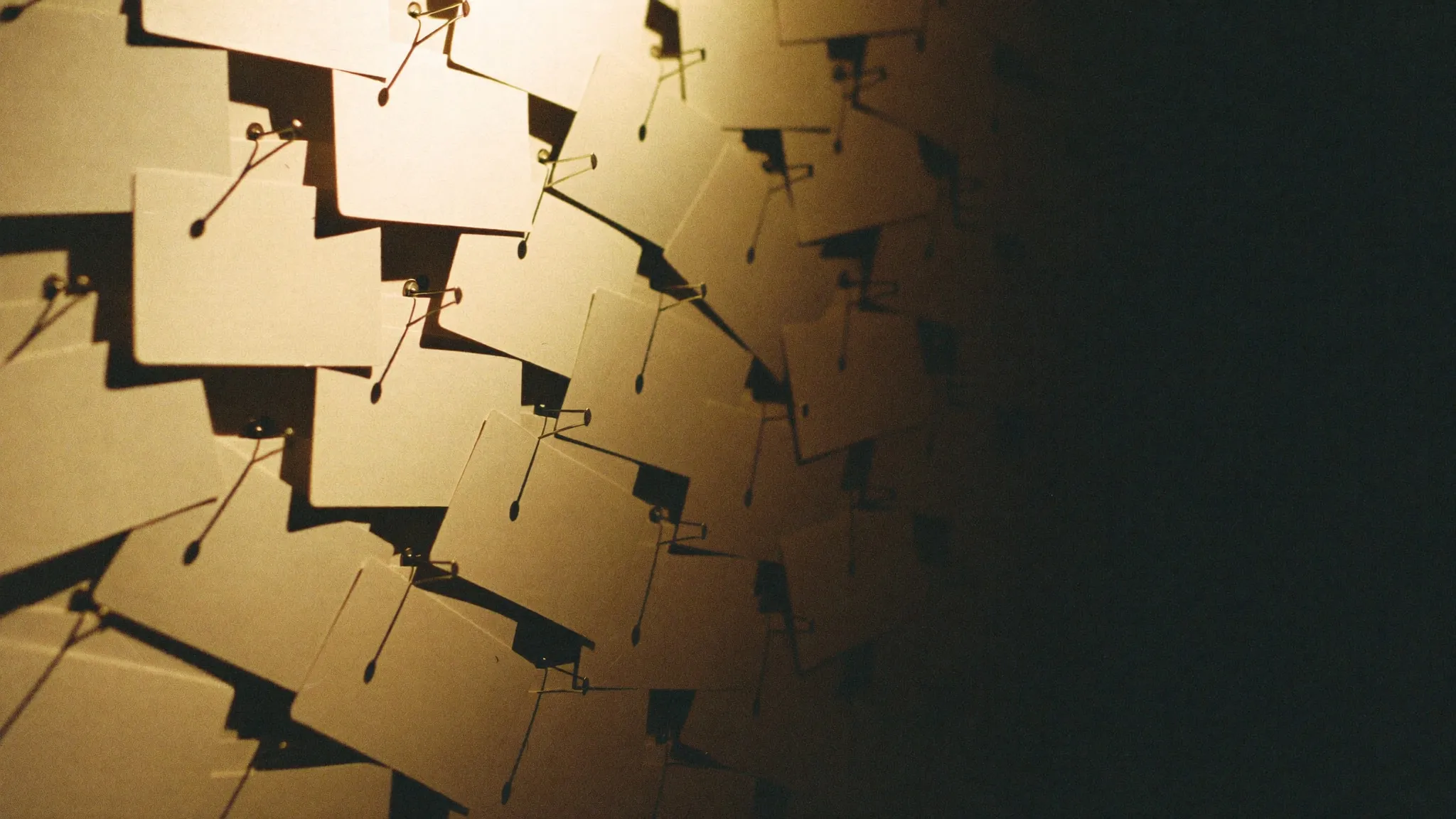 A wall densely layered with blank pinned index cards, lit from one side and falling away into shadow.